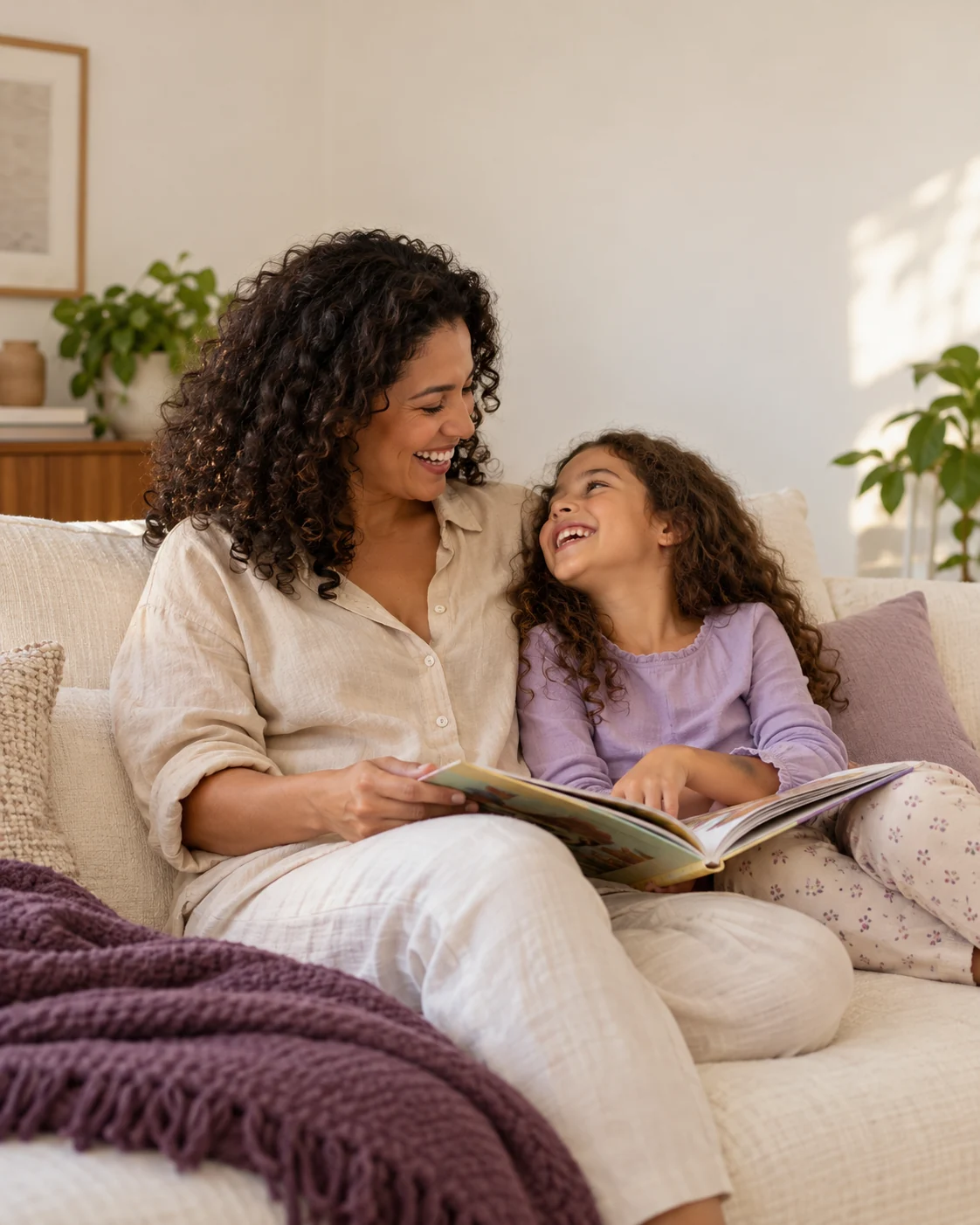 Mãe e filha sorrindo enquanto compartilham um livro no sofá de casa